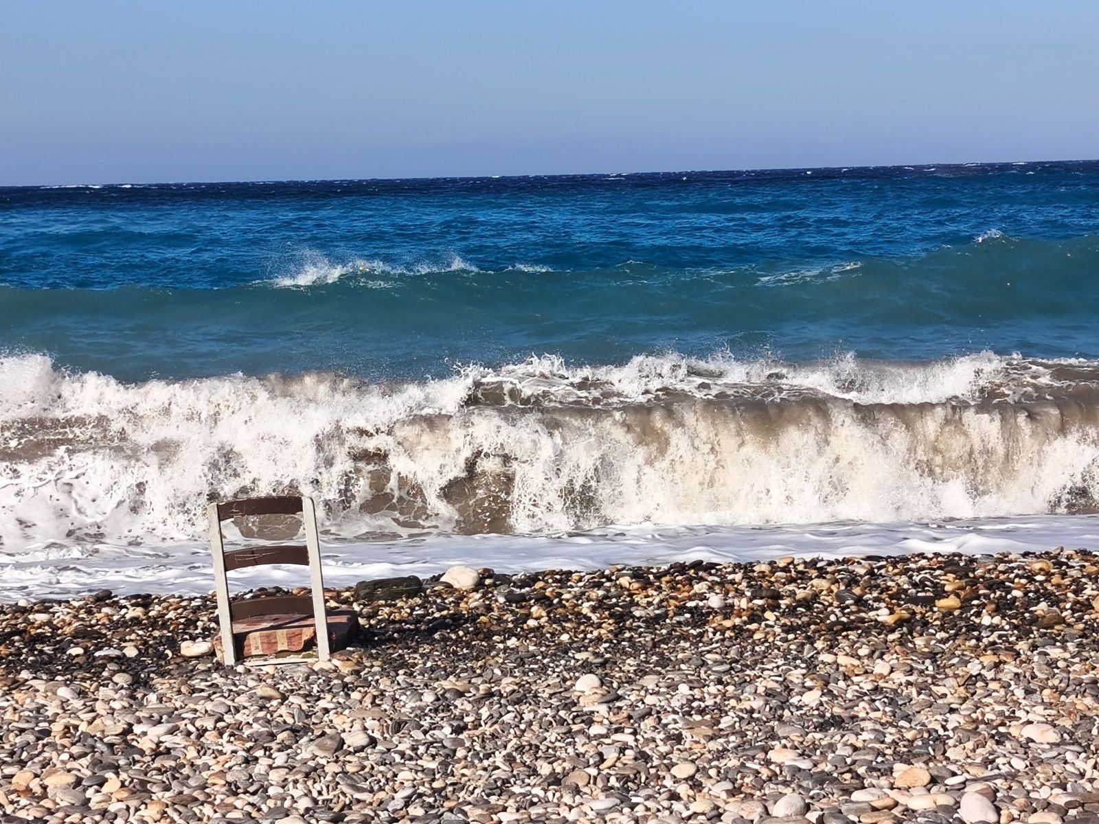 Ξύλινη καρέκλα σε παραλία με φουρτουνιασμένη θάλασσα