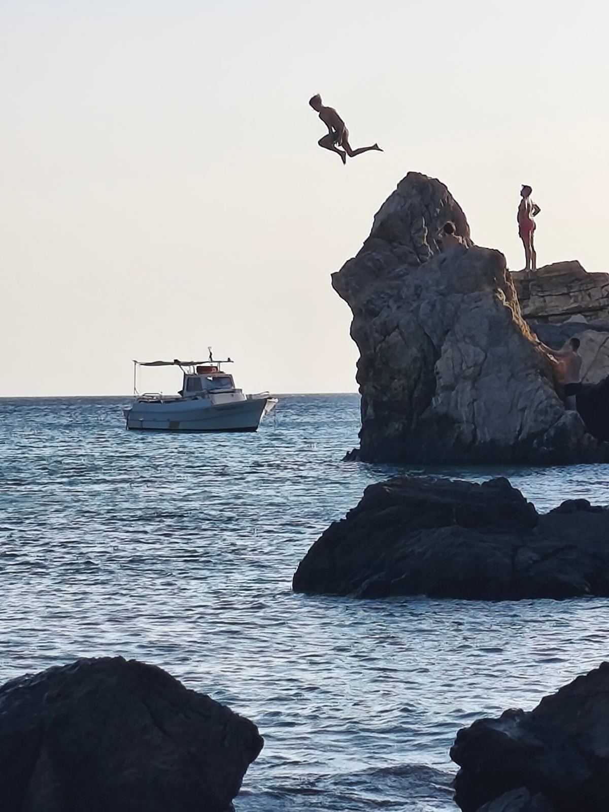 Βουτιά από βράχο στη θάλασσα με βάρκα στο βάθος