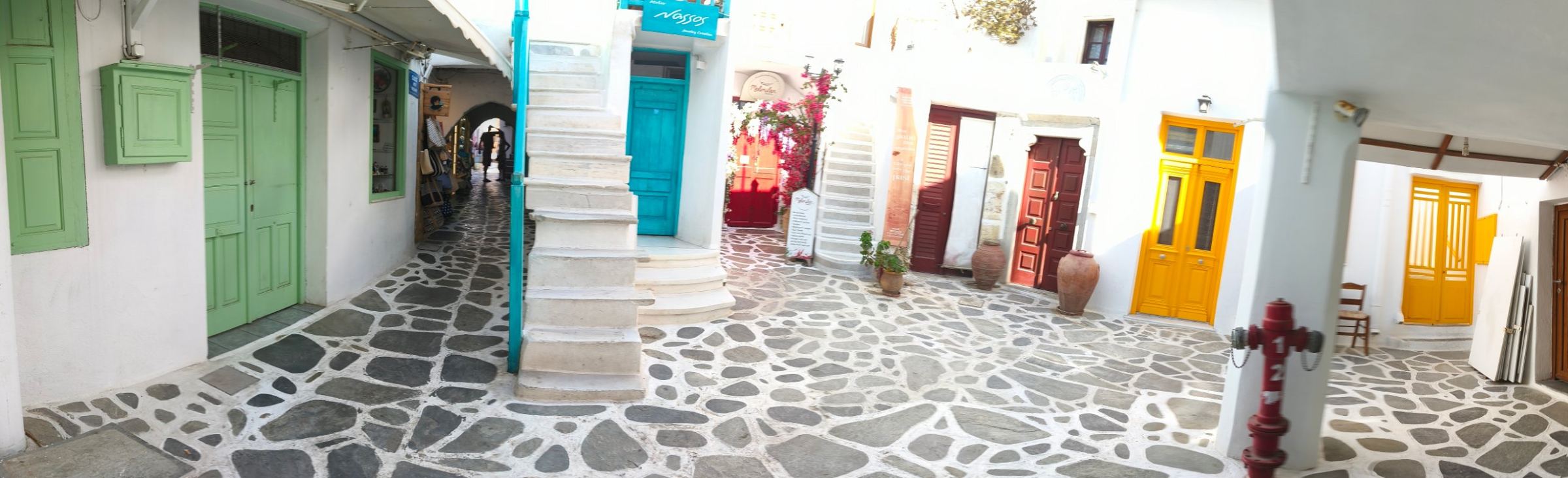 Πλακόστρωτη αυλή με χρωματιστές πόρτες σε νησιώτικο χωριό